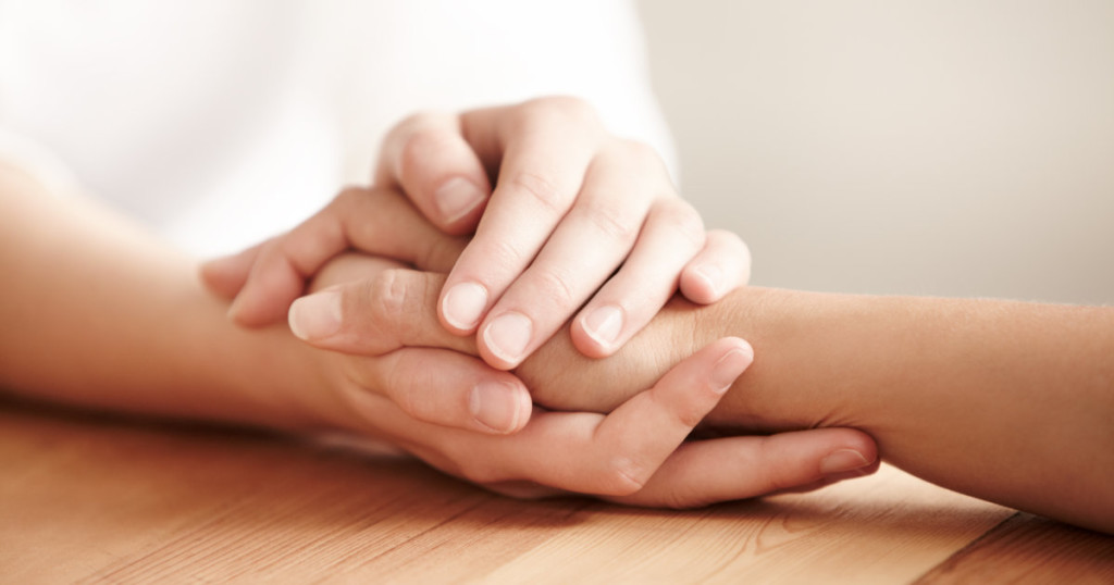 Hands holding one another on a table in prayer